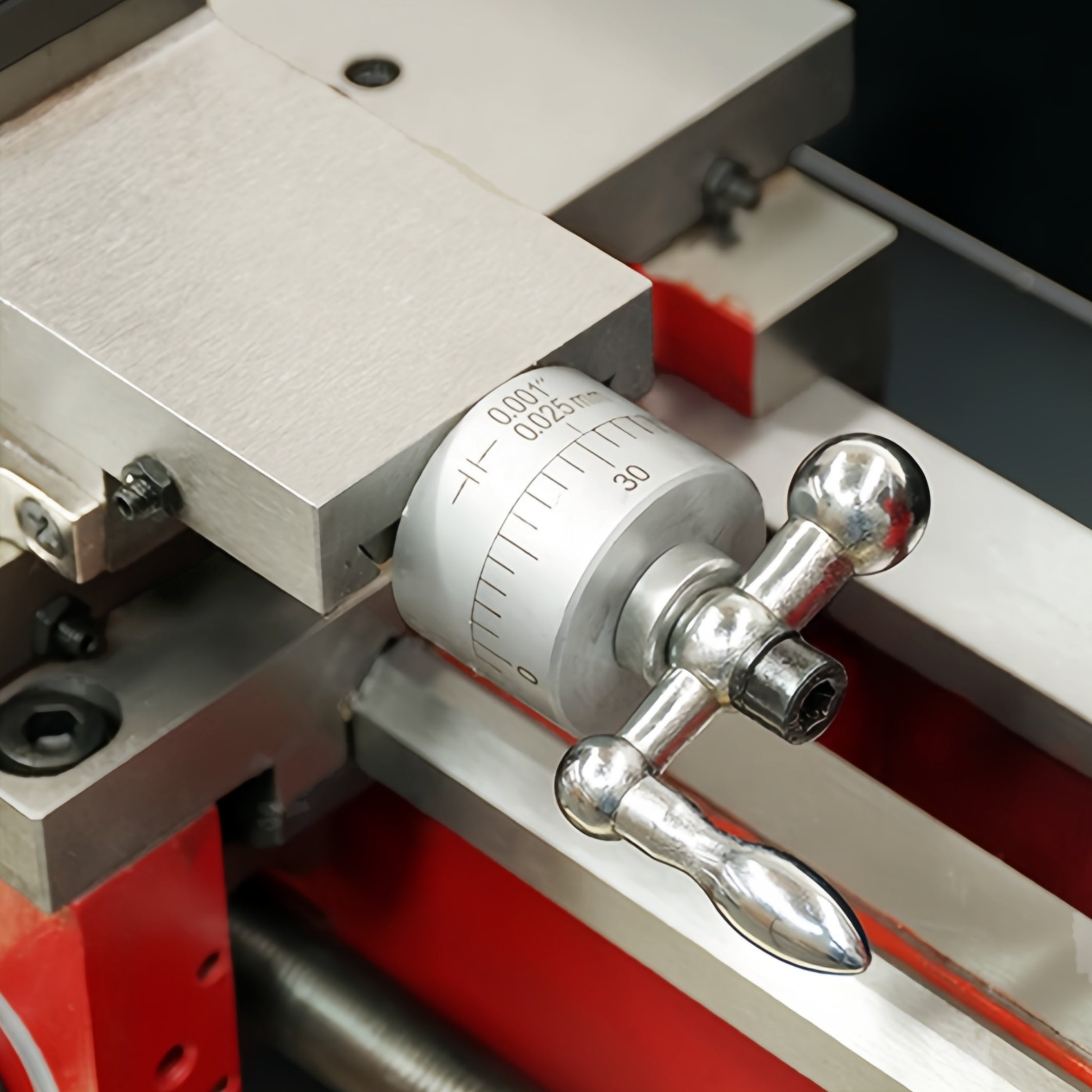 Close-up of a precision metal dial caliper or measuring device with silver metallic components, a white measurement scale ring, and red support blocks.