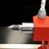 Close-up of a precision machined metal dial indicator or measuring tool with a pointed silver tip, a silver scale barrel marked 0-10-20 mm, and a bright red mounting block against a dark background.