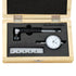 A precision dial indicator set inside an open light wood presentation box with black foam insert. The set includes a dial indicator, a caliper-like measuring tool, a small ruler scale, and a black pointer.
