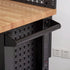 Close-up of a black metal shelving unit with a light wood countertop, perforated back panel, pull-out shelf tray, and vertical power outlets against a white wall.