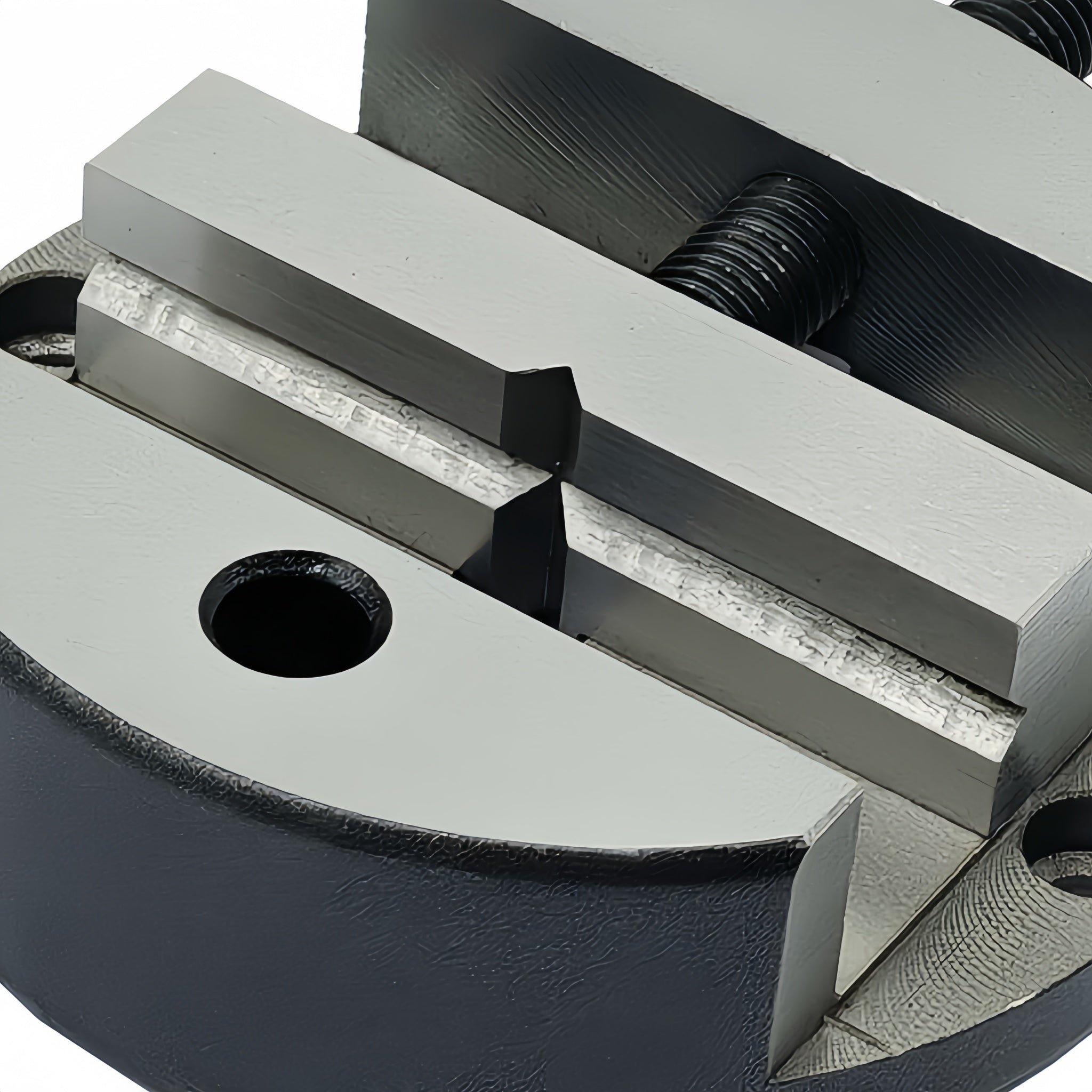 Close-up of a heavy-duty metal clamp or vise with a matte black body and silver-gray machined surfaces, showing threaded components and a circular hole on the front.