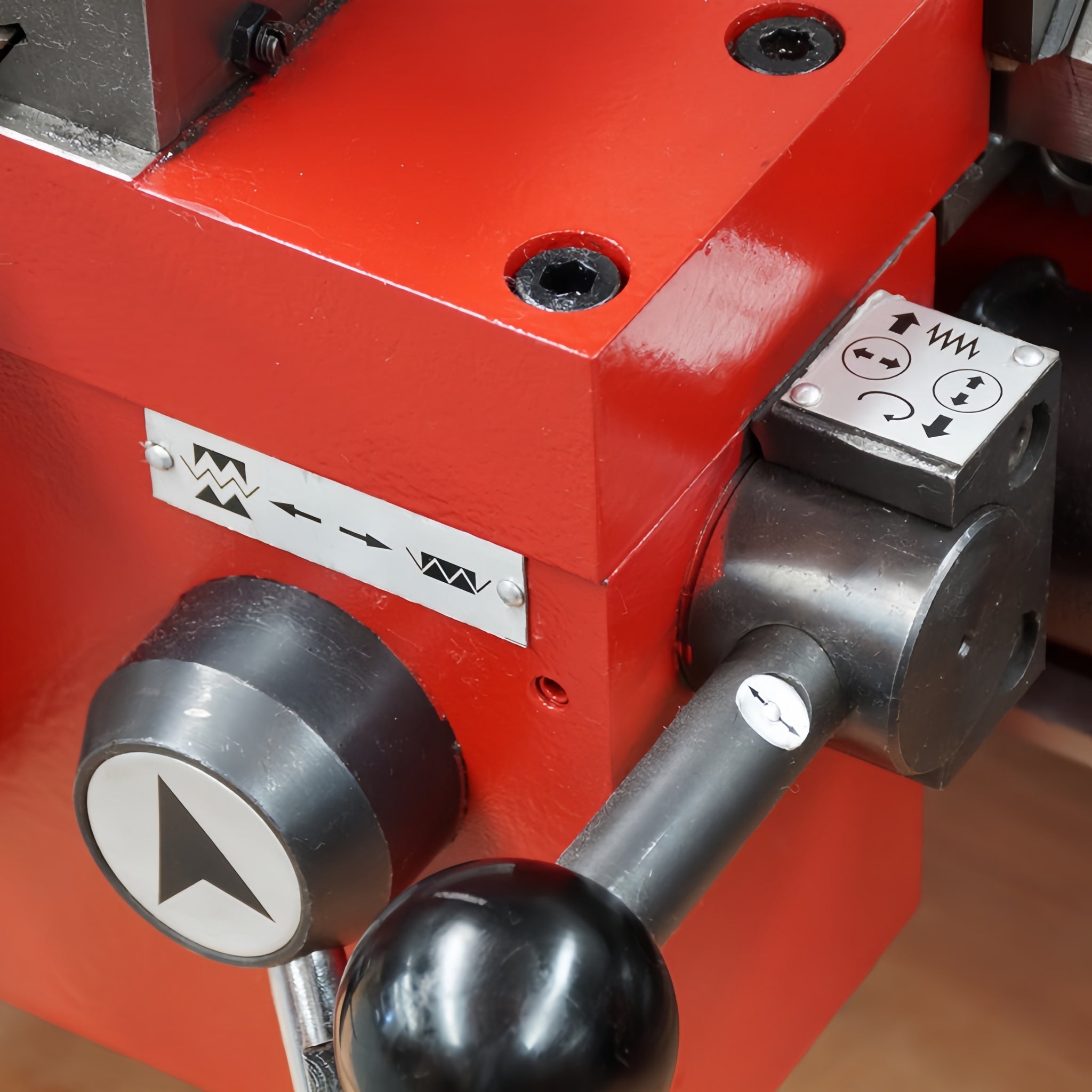 Close-up of a red industrial machine component with black control levers, a metal control box, and printed control symbols on a white label.