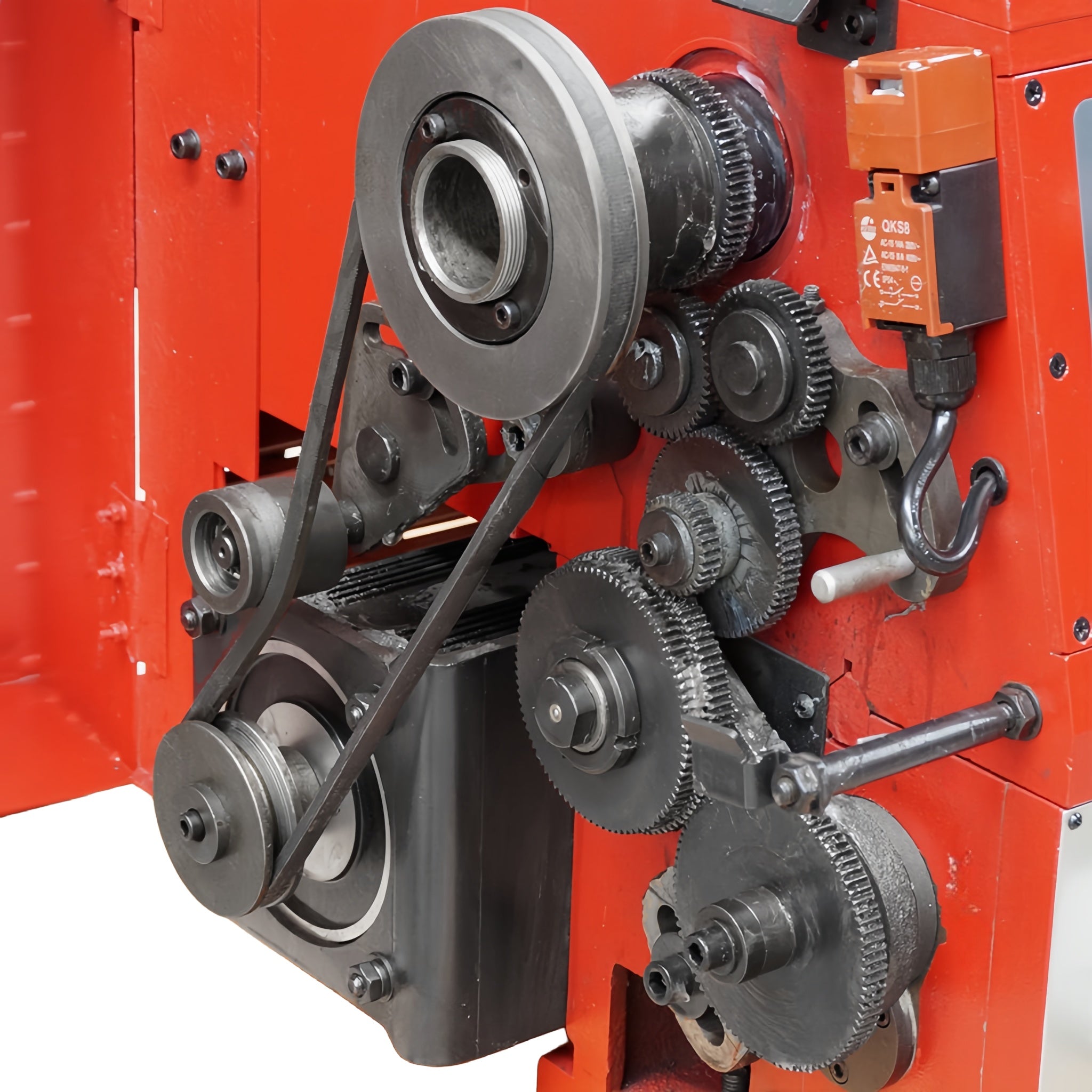 Close-up of a red industrial machine with metal gears, pulleys, belts, and an orange electrical component mounted on the side.