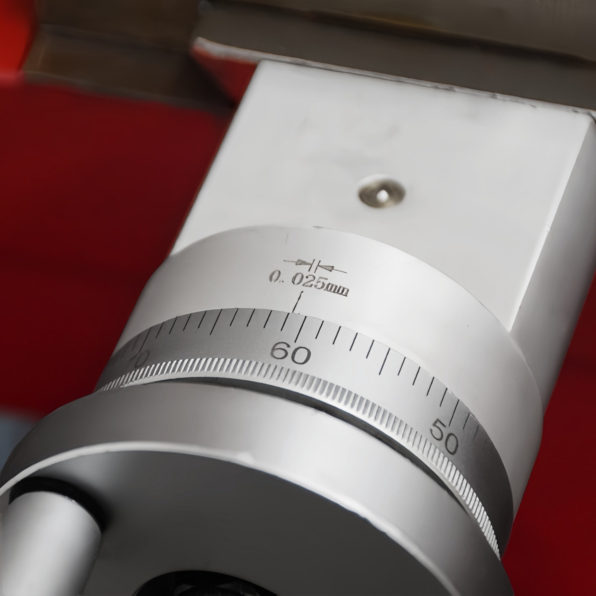 Close-up of a metallic precision dial or caliper component with a silver-toned ring, black measurement markings, and a red background.
