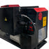 A close-up of a black industrial machine or equipment housing with red panels, warning labels, a power cord plugged in, and a small control switch on a white background.