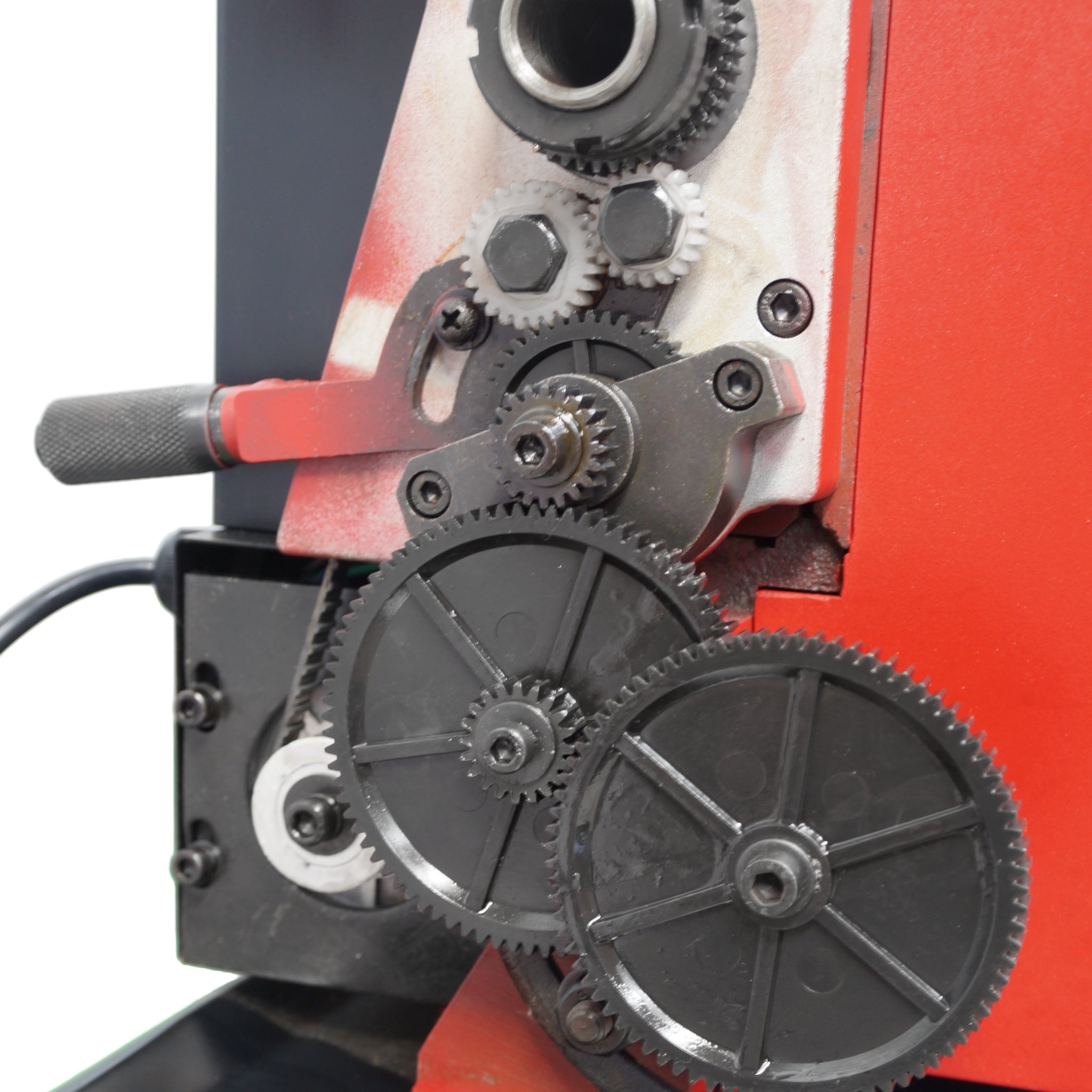 Close-up of a red and black mechanical device with interlocking black gears, metal sprockets, and a red handle on a white background.