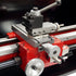 Close-up of a red and silver metal lathe machine component with a carriage, quick change tool post, and a handwheel on a dark background.