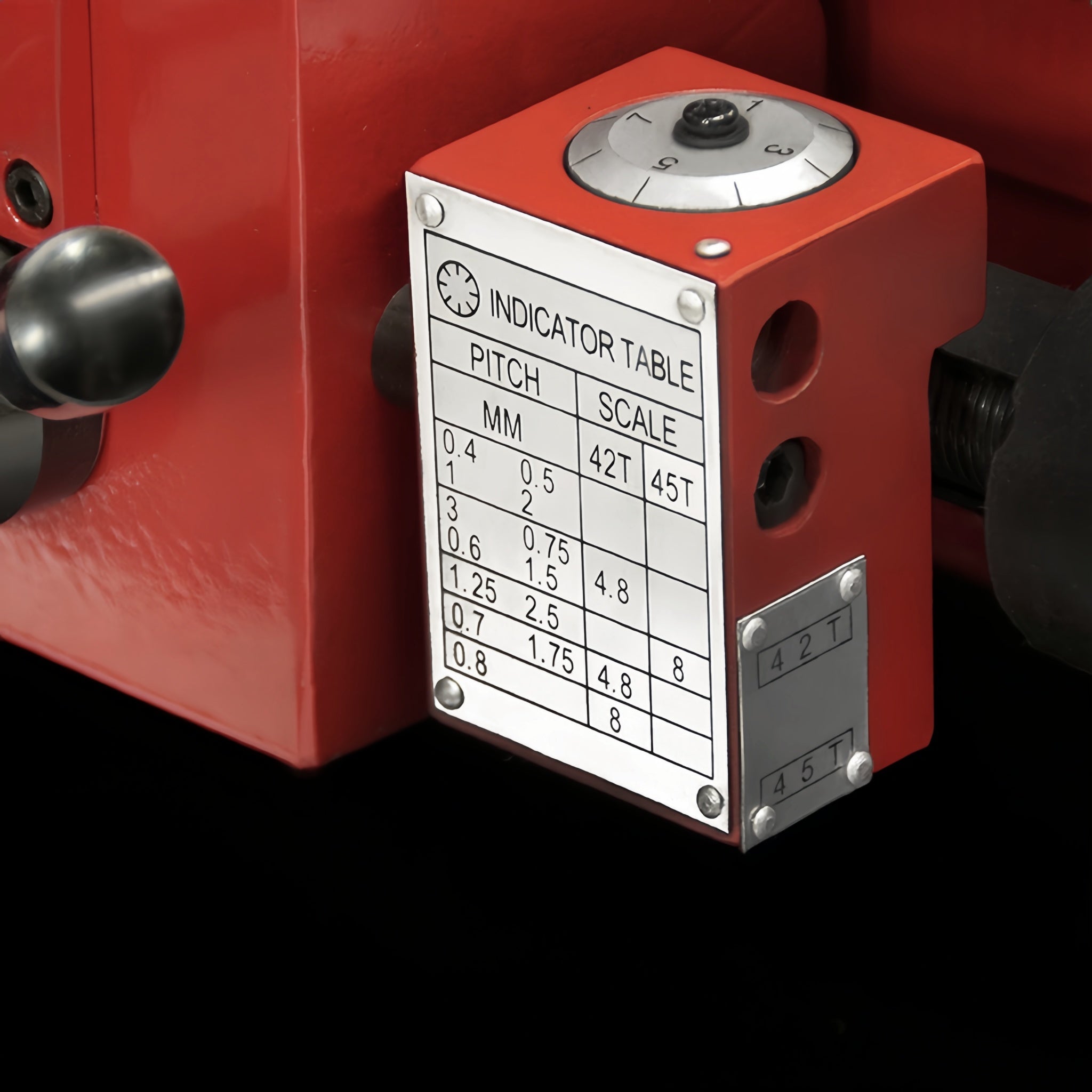 A close-up of a red industrial machine component with a metal indicator table plate showing pitch and scale measurements, mounted against a black background.