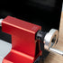 Close-up of a red and silver metal lathe tailstock adjustment component with a black rotary dial and white measurement markings, shown against a dark and light background.