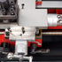Close-up of a precision mechanical tool or machine component with silver metal parts, red housing, threaded rods, and white measurement scales. A watermark reading 'Musc Machines & Tools' appears across the bottom.