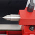 Close-up of a machined metal dial indicator or precision measuring tool with a pointed silver tip and engraved scale, mounted on a bright red clamp or fixture.