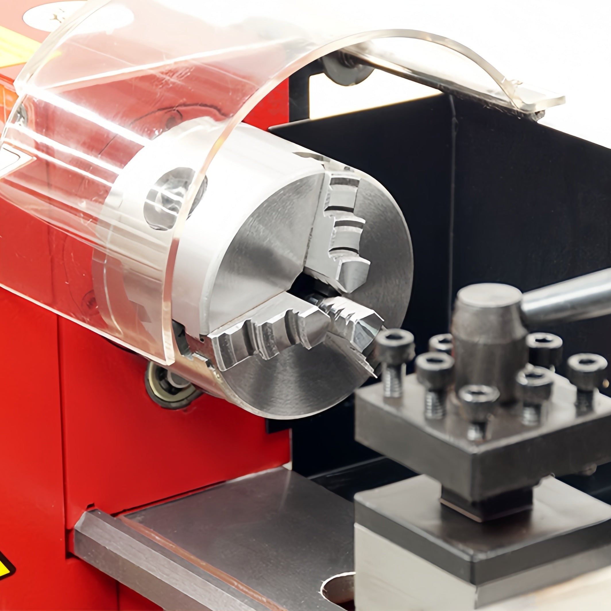 Close-up of a metal lathe or milling machine spindle and chuck assembly with a transparent protective guard, mounted on a red machine body.
