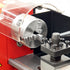 Close-up of a metal lathe or milling machine spindle and chuck assembly with a transparent protective guard, mounted on a red machine body.