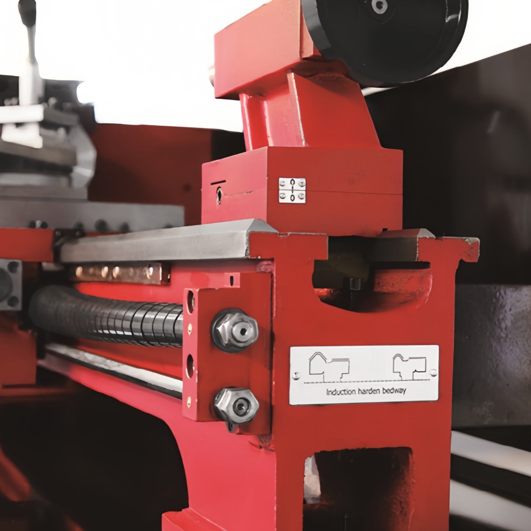 Close-up of a red industrial machine component with a black curved hose, metal rails, and a white label reading 'Induction harden bedway'.